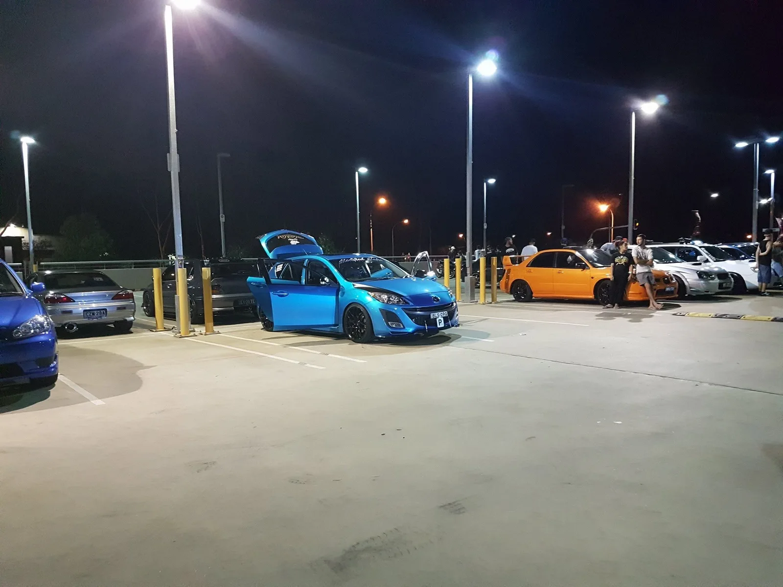People gathered among a mixed group of cars at night